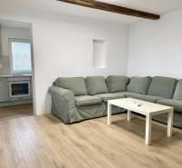 Wohnzimmer mit Ecksofa, Holzboden und Küche in einem Einfamilienhaus.