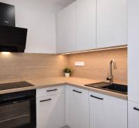 Küche in einer 2-Zimmer-Wohnung mit Holzdekor, weißen Schränken und einem schwarzen Spülbecken.
