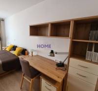 Schreibtisch mit Regalen, Bett und Boden mit Holzdekor in einer 2-Zimmer-Wohnung.