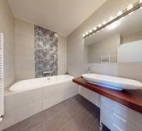 Badezimmer in einer 3-Zimmer-Wohnung mit Badewanne, Spiegel und gemusterten Fliesen über der Badewanne.
