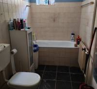 Badezimmer mit Badewanne und Toilette in einem Einfamilienhaus, mit dunklen Fliesen und einem Fenster.