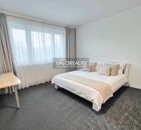 Schlafzimmer mit hellem Bett und Tisch in einer 4-Zimmer-Wohnung, weiße Wände und grauer Teppich.