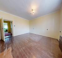 Ein Zimmer mit einem Holzboden, hellen Wänden und einem Fenster mit weißem Vorhang.