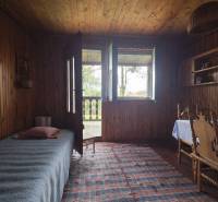 Innenraum einer Hütte mit Holzeinrichtung, Bett, Tisch, Stühle und Teppich.