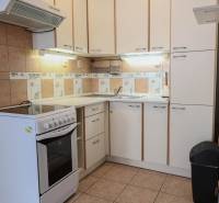 Küche in einer 2-Zimmer-Wohnung mit weißen Schränken und Herd, Boden mit Holzdekor.