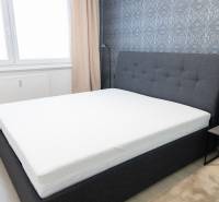 Schlafzimmer mit grauem Bett, gemusterten Tapeten und Nachttisch.