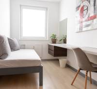 Ein Zimmer in einer 4-Zimmer-Wohnung mit einem Bett, einem Tisch und einem Boden in Holzoptik.