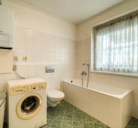 Badezimmer in einer 3-Zimmer-Wohnung mit Waschmaschine, Badewanne und Fenster, geflieste Wände.