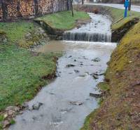 Ein Bach, der durch die Erholungsgebiete in Púchov fließt, mit Holz, das am Rand gelagert ist.