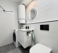 Badezimmer in einer Einzimmerwohnung mit Waschmaschine, Boiler und Spiegel in einem runden Rahmen.