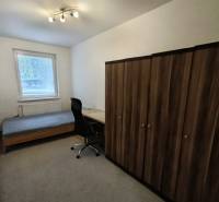 Ein Zimmer in einer 4-Zimmer-Wohnung mit einem Bett, einem Tisch, einem Stuhl und einem Schrank auf dem Teppich.