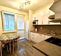 Küche in einer 4-Zimmer-Wohnung mit Holzboden, weißen Schränken und Essecke.