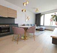 Wohnzimmer mit Küche, Boden mit Holzdekor, helle Couch, Esstisch, Blumen.