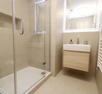 Badezimmer mit verglaster Duschkabine und hellem Waschbecken in einer 2-Zimmer-Wohnung.