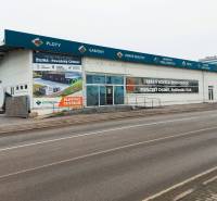 Geschäftsräume in der Kamenna-Straße in Žilina mit Werbeaufschriften und einem leeren Parkplatz.