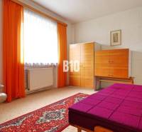 Ein Zimmer mit Teppichboden, einem cremefarbenen Sessel, einem bunten Bett und einem Schrank in einem Einfamilienhaus.