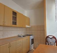 Küche mit hellen Möbeln, Herd und Tisch in einer 3-Zimmer-Wohnung.