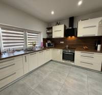 Küche in einem Einfamilienhaus mit großen Fenstern und eingebauten Geräten, Boden mit Holzdekor.