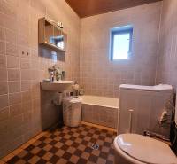 Badezimmer in einem Einfamilienhaus mit Badewanne, Waschbecken und Waschmaschine, Fliesen im Schachbrettmuster.