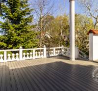 Terrasse mit Holzboden, umgeben von Grün und Balkongeländer.