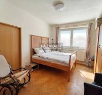 Ein Zimmer in einer 3-Zimmer-Wohnung mit einem Bett, einem Tisch, einem Boden in Holzoptik und gelben Wänden.