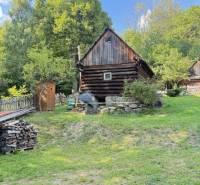 Eine Holzhütte in Horná Mariková, umgeben von Grün und Holzstapeln.