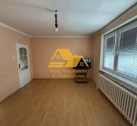 Ein Zimmer in einem Einfamilienhaus mit weißen Wänden, einem Boden in Holzoptik und einem Fenster mit Jalousien.