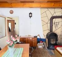 Innenraum eines Einfamilienhauses mit Kachelherd, Holzbalkendecke und Esstisch mit Blumen.