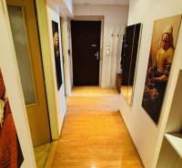 Ein enger Flur mit Holzboden in einer 3-Zimmer-Wohnung, mit Bildern und einem Spiegel.