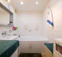 Badezimmer in einer 3-Zimmer-Wohnung mit Badewanne, Waschbecken, weißen Fliesen und grünem Teppich.