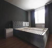 Schlafzimmer mit einem dunkelgrauen Bett, einem Nachttisch und einem Boden mit Holzdekor in einer 3-Zimmer-Wohnung.