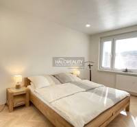 Helles Schlafzimmer in einer Einzimmerwohnung mit Holzboden und großem Fenster.