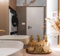 Badezimmer mit Waschbecken, goldenen Spendern und dekorativer natürlicher Dekoration in einer 3-Zimmer-Wohnung.