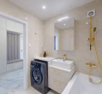 Badezimmer in einer 3-Zimmer-Wohnung mit Waschmaschine, Waschbecken und Badewanne mit goldenen Accessoires.