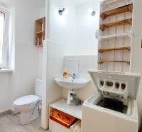 Badezimmer in einer 2-Zimmer-Wohnung mit Waschmaschine, Sanitäranlage und Regal für Handtücher.