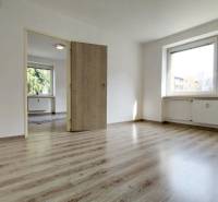 Zweizimmerwohnung mit Holzboden, großem Fenster und weißen Wänden.