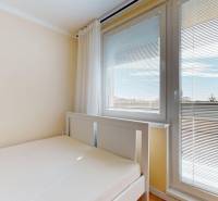 Bett in einer Einzimmerwohnung mit Blick durch die Jalousien am Fenster.