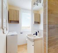 Badezimmer in einer Einzimmerwohnung mit Dusche, Waschmaschine und Boden mit Holzdekor.