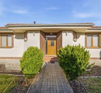 Ein Einfamilienhaus in Kútniky mit Strauchbepflanzung, weißer Fassade und braunen Akzenten.