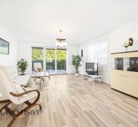 Helles Wohnzimmer mit Holzboden, Sofa, Sessel und Fernseher.