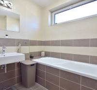 Badezimmer mit Badewanne und Waschbecken in einer 3-Zimmer-Wohnung mit beigen Fliesen.