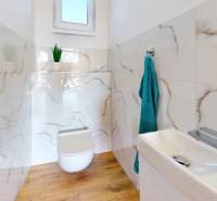Ein Badezimmer in einem Einfamilienhaus mit einem Boden in Holzoptik und Wänden mit Marmorverkleidung.