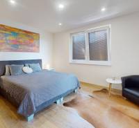 Schlafzimmer in einem Einfamilienhaus mit Bett, Sessel und Boden mit Holzdekor.