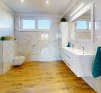 Badezimmer in einem Einfamilienhaus mit einem Boden in Holzoptik und Fliesen in Marmoroptik.