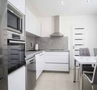 Küche in einer 2-Zimmer-Wohnung mit glänzenden Geräten, grauen Wänden und einem Esstisch.