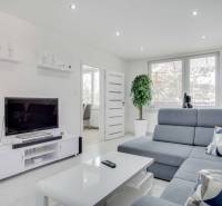 Wohnzimmer in einer Zweizimmerwohnung mit Fernseher, grauem Sofa und weißen Möbeln.