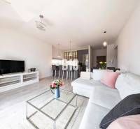 Wohnzimmer in einer 3-Zimmer-Wohnung mit Holzboden, weißem Sofa und Fernseher.