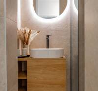 Badezimmer in einer 3-Zimmer-Wohnung mit einem Waschbecken auf einem Holzschrank und einem Spiegel mit Beleuchtung.