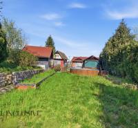 Gärten in Kráľová nad Váhom mit einem Häuschen, dichter Vegetation und Rasen unter blauem Himmel.