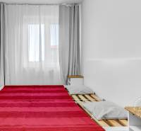 Schlafzimmer in einer 2-Zimmer-Wohnung mit einem Bett mit grauen Kissen, einer Decke und einem Nachttisch.